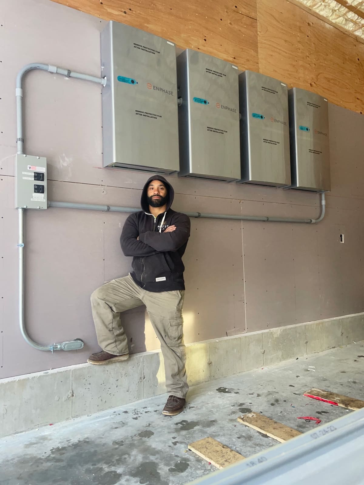 Micah Gentile, owner and licensed electrician at Powered Up LLC, standing in front of Enphase battery backup installation